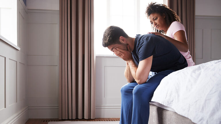 Woman sat on bed comforting man suffering with anxiety disorder