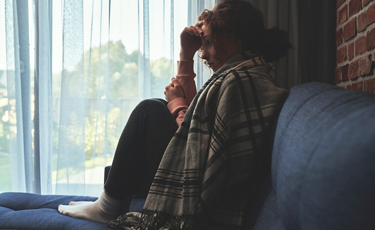 Woman sat on sofa struggling with symptoms of MUS